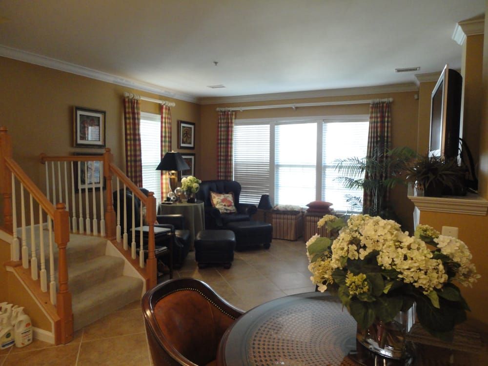 Living room with armchairs, large windows, stairs, and a table with a vase of white flowers in the foreground.