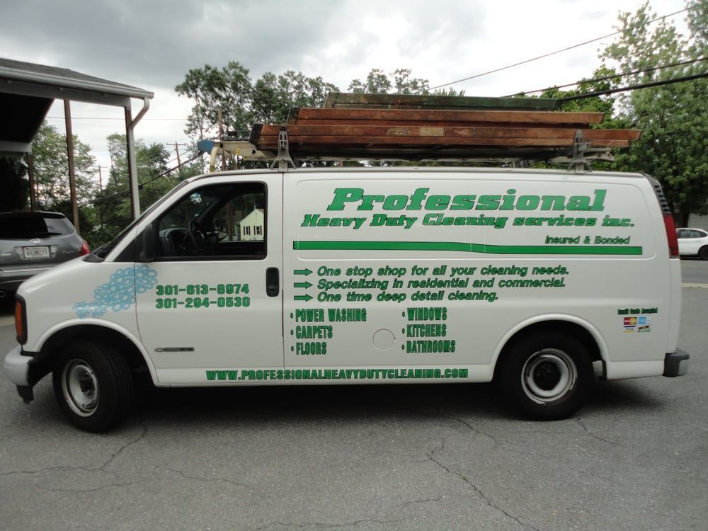 White van with “Professional Heavy Duty Cleaning Services” logo and contact info, ladders on roof, parked on street.