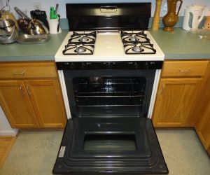 A gas stove with four burners and an oven below, oven door open, surrounded by kitchen counters and appliances.