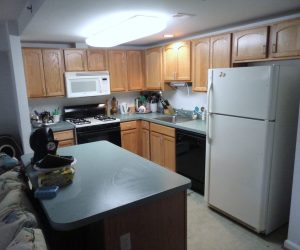 Kitchen with wooden cabinets, white fridge, stove, microwave, dishwasher, and cluttered countertop with various items.