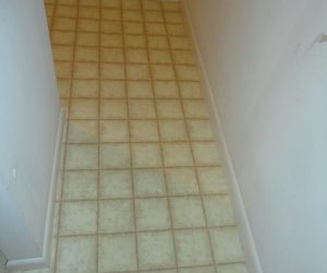 A narrow hallway with white walls and a beige checkered linoleum floor.
