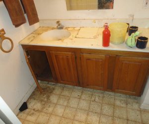 Dirty bathroom with a stained countertop, open cabinet door, and grimy floor tiles.
