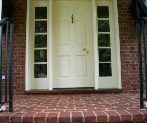 White front door with sidelights, brass knocker, and brick steps with black metal railings on both sides.