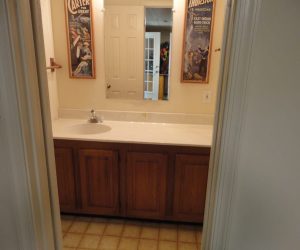 Bathroom with a single sink, wooden cabinets, a large mirror, and two vintage posters on the walls.