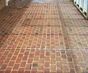 Red and brown brick patio with visible grout lines and a hint of patio furniture in the upper left corner.