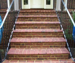 Six brick steps with black metal railings on both sides lead up to a white double door entrance.