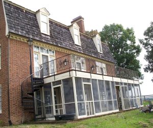 Brick house with screened porch, upper deck, and spiral staircase, set beside a tree and grassy yard.