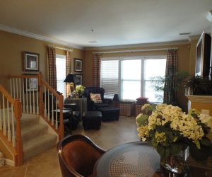 Living room with armchairs, large windows, stairs, and a table with a vase of white flowers in the foreground.
