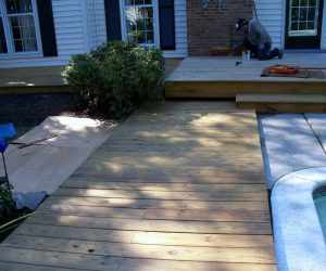 A person works on a wooden deck beside a house; a pool and shrubbery are also visible in the scene.