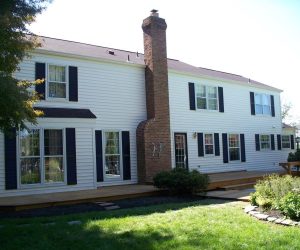 Two-story white house with black shutters, brick chimney, large windows, and a wooden deck in the backyard.
