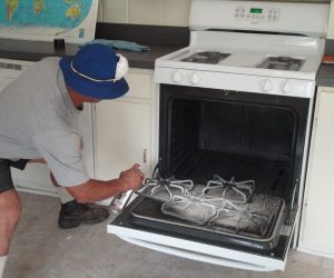 Person cleaning stove grates inside an open oven with spray cleaner in a kitchen.