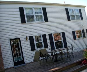 A two-story house with white siding, black shutters, and patio furniture on a wooden deck.