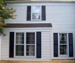 White house exterior with three windows, black shutters, horizontal siding, and a tree partially visible on the left.