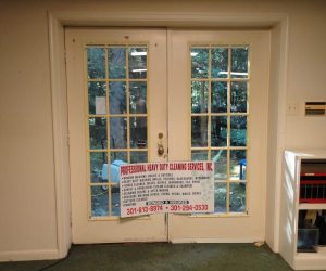 A double glass door with a cleaning service banner attached, seen from inside a room with carpet and shelves.